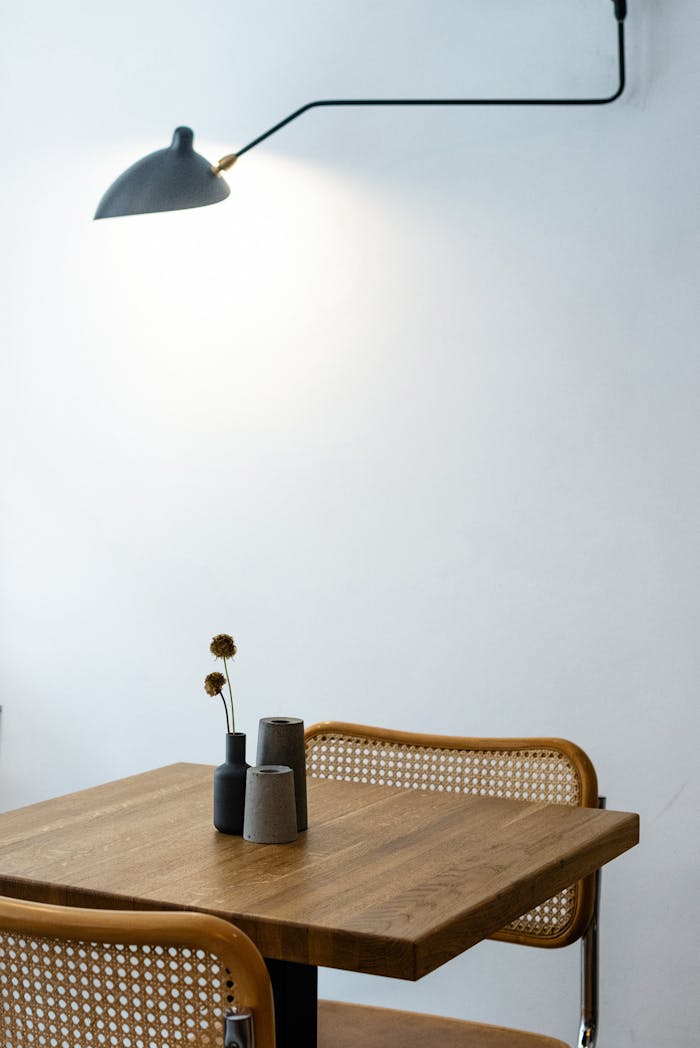Mastering the First Impression: Your intriguing post title goes here Square shaped wooden table with decorative flower and wicker chairs back and hanging lamp turned on near white wall in flat